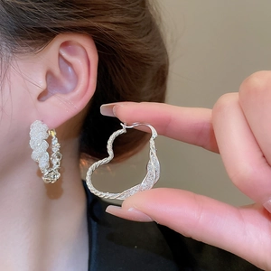 Detailed view of silver heart earrings with braided texture and zircon micro-pave