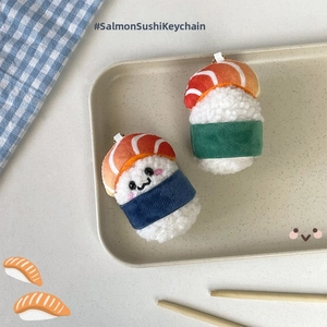 Detailed plush salmon sushi charms with cute embroidery displayed on a dining plate