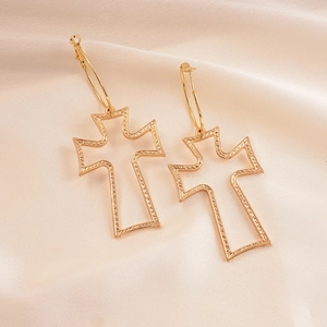 Detail view of golden textured hollow cross hoop earrings on soft pink satin fabric