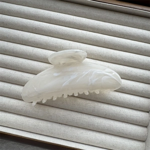 Close-up of ink-painted cream marble hair claw clip on beige velvet display tray