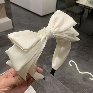 Close-up of a beige fabric headband featuring a large elegant triple-layered bow design