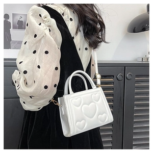 Sac à main blanc carré avec motif cœur en relief et boucles dorées porté par un mannequin