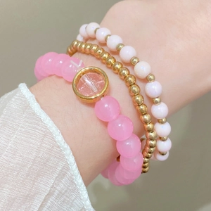 Detail of layered handmade beaded bracelets with pink quartz charm and gold beads