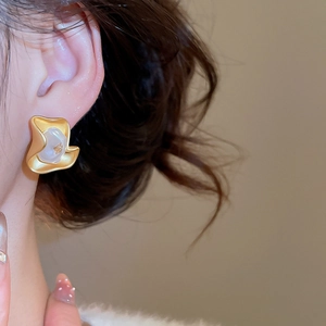 Close-up of gold irregular floral earring with white pearl petal on a female model