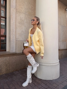 Detail of light yellow knit cardigan paired with a white dress and boots in an urban setting