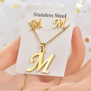 Primo piano del set di gioielli in acciaio inossidabile dorato con collana e orecchini lettera M