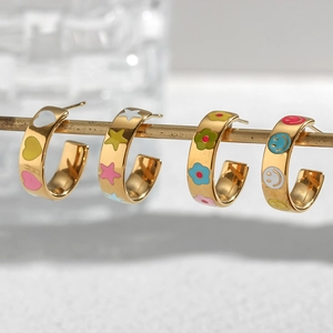 Close-up of gold C-shaped earrings with colorful enamel hearts and smileys