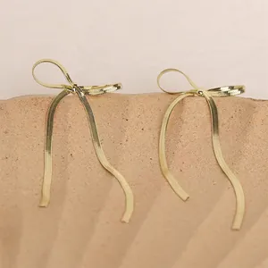 Minimalist golden bow stud earrings with textured snake chain on stone display