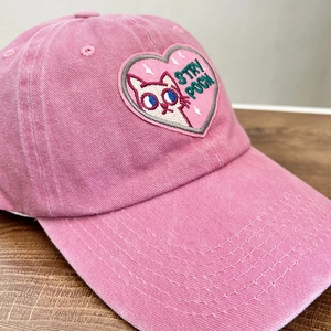 Pink washed cotton baseball cap featuring vintage cat embroidery on a wooden table