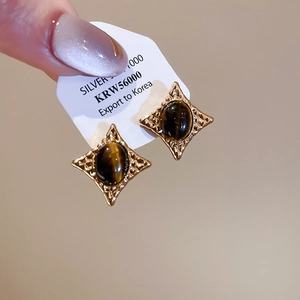Close-up of vintage gold star-shaped earrings with oval tiger eye stones on white cards