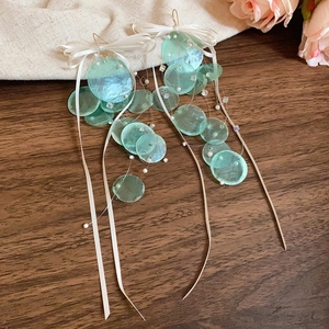 Detail of light green shell earrings with white ribbon bows on a dark wooden background