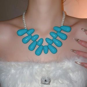 Détail d'un collier imposant avec gouttes turquoise et perles blanches sur le modèle