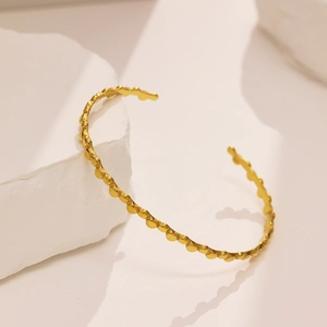 Close-up of golden C-shaped stainless steel bracelet with unique beaded texture detail