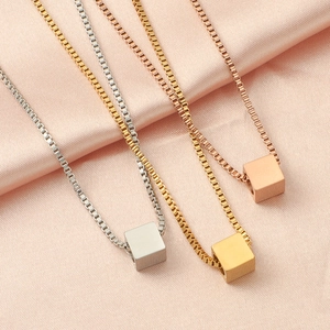 Detailed view of three minimalist cube necklaces in silver, gold, and rose gold on pink silk