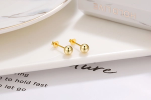 Macro shot of polished gold-plated ball earrings with S925 hallmark on a ceramic tray