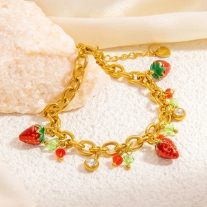 Macro shot of gold strawberry charm bracelet with colorful beads and crystals on silk fabric