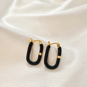 Detailed close-up of U-shaped gold earrings with black drip oil on white silk background
