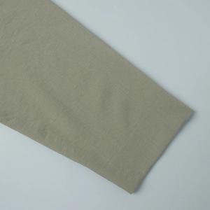 Close-up of olive green linen fabric texture and stitching detail on shirt sleeve hem