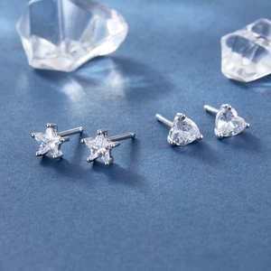 Detailed view of silver heart and star stud earrings with clear zircon on blue background