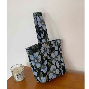 Detail of blue floral jacquard handbag with metal snap button on a wooden surface