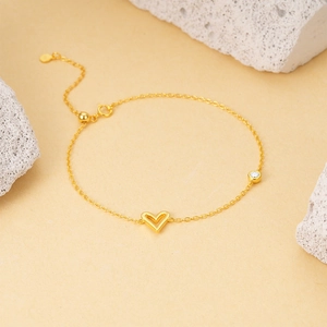 Detail of gold heart charm bracelet with sparkling diamond accent on natural stone background