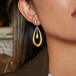 Polished two-tone stainless steel teardrop earrings worn by a model in a close-up side view