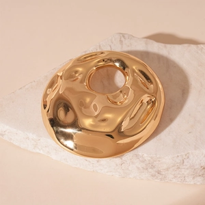 Detail of a golden hammered metal brooch with abstract wavy texture and mirror finish