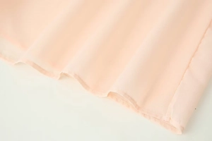 Détail de l'ourlet de la chemise rose pâle avec coutures précises et tissu transparent