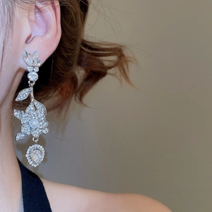Dettaglio di orecchini pendenti in argento con cristalli brillanti e perla a goccia