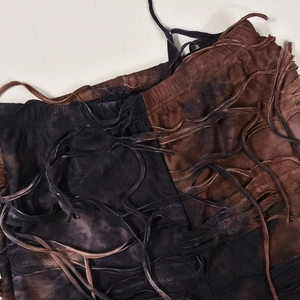 Dettaglio dei pantaloni a zampa tie-dye marroni con frange e particolari lacci intrecciati