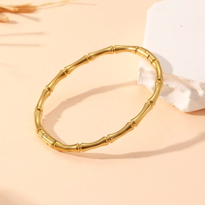 Detail view of a vintage golden bamboo style bracelet on a minimalist textured background