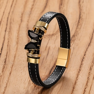 Détail d'un bracelet en cuir noir avec papillons dorés et cristaux sur fond bois