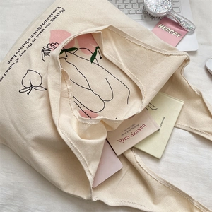 Detail of minimalist cream canvas tote bag with peach doodle and laptop on bed
