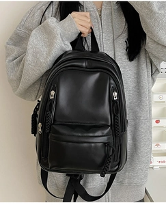 Detail view of a black minimalist PU leather backpack featuring woven zipper pulls