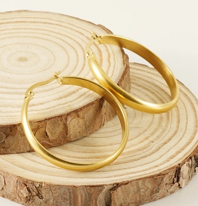Detailansicht matter 18K Gold-Creolen auf rustikalen natürlichen Holzscheiben liegend