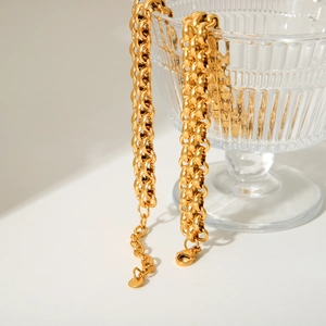 Macro detail of gold-plated woven mesh chain necklace on a glass cup rim