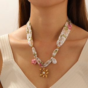 Detail of floral ribbon necklace with gold flower, pearl, and pink charms on a model