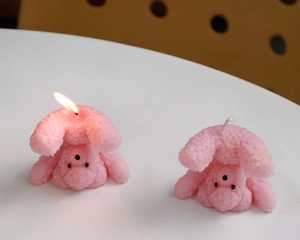 Detail view of pink poodle shaped scented candles with one candle burning on a white surface