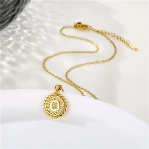 Detailed view of golden round pendant with letter O and beaded edge on white plate