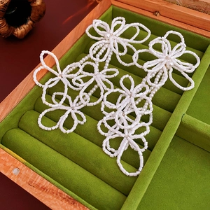 Detailed close-up of handmade white beaded flower earrings resting in a green wooden box