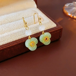Macro detail of gold-plated flower earrings with green jade stones and red zircon accents