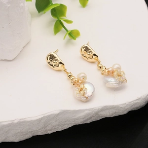 Baroque pearl drop earrings with 18k gold plating and crystals on a white stone background