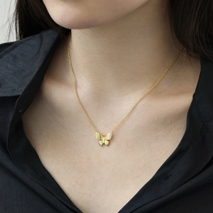 Detail shot of a golden butterfly pendant necklace worn on a black shirt for contrast