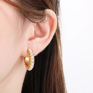 Close-up of elegant C-shaped gold hoop earrings with inlaid white pearls on a model