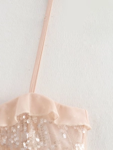 Macro view of light pink sequined fabric with ruffle trim and thin spaghetti straps