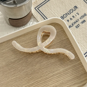 Detail of twisted pearlescent white acetate hair claw clip with golden spring on tray