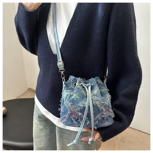Detail of denim bucket bag with colorful star patterns and frayed edges on shoulder strap