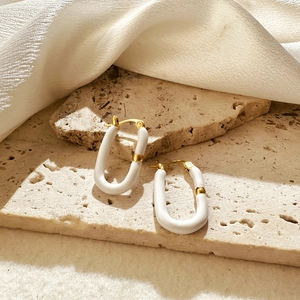 Detailed close-up of U-shaped white enamel and gold plated earrings on stone texture