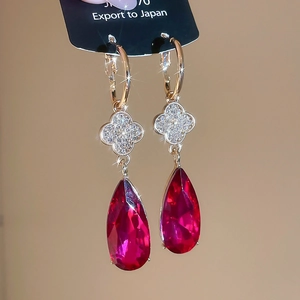 Macro shot of gold-plated drop earrings with red pear-cut gems and clover details