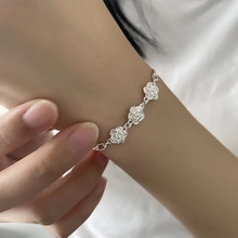 Detail of silver bracelet featuring three hollow rose charms worn on a wrist